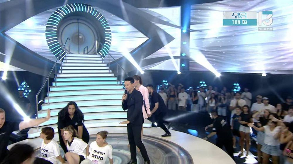 TV set with Big Brother eye and people in t-shirts sitting on the floor 