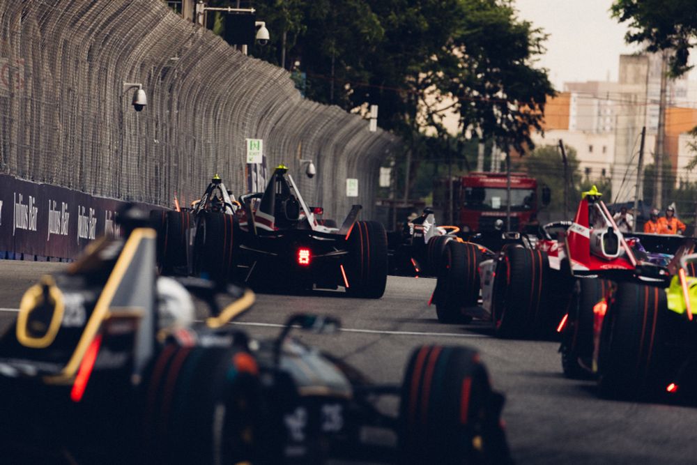 A pack of Formula E racecars are seen racing away from the camera. The car closest to the camera is out of focus, while the cars further along in the pack are sharp.