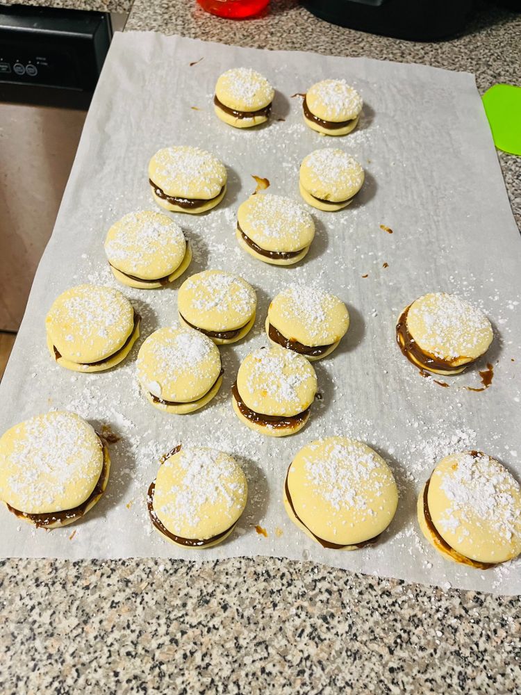 16 homemade alfajores on a sheet of parchment paper with powdered sugar on top