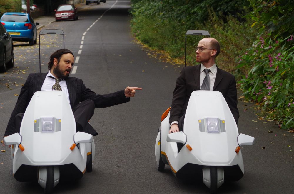 Two businessmen driving Sinclair C5 vehicles from the 1980s.