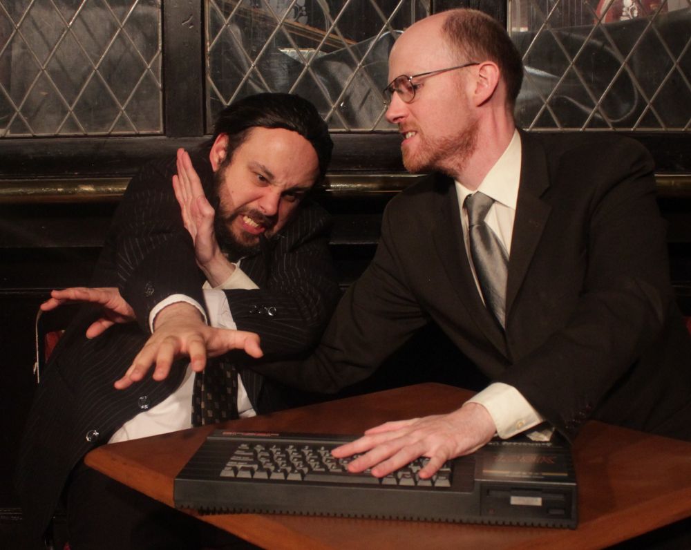 Two businessmen sitting in a bar, fighting over an 80s-style computer keyboard.