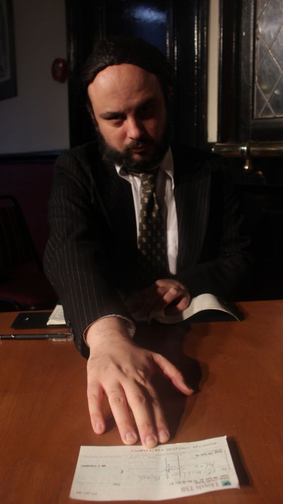 A businessman at a desk, pushing a cheque towards you/the camera.