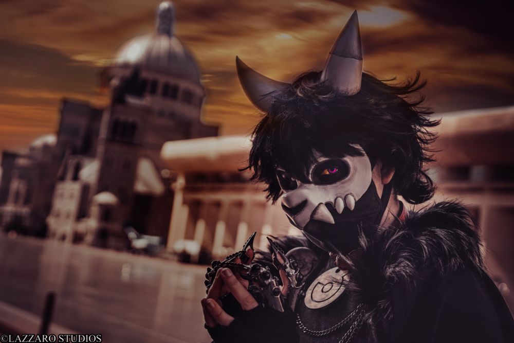 Shibalove Cosplay as King Clawthorne poses in front of an older government building, posing with their hands together deviously. The photo has a sepia tone to it
