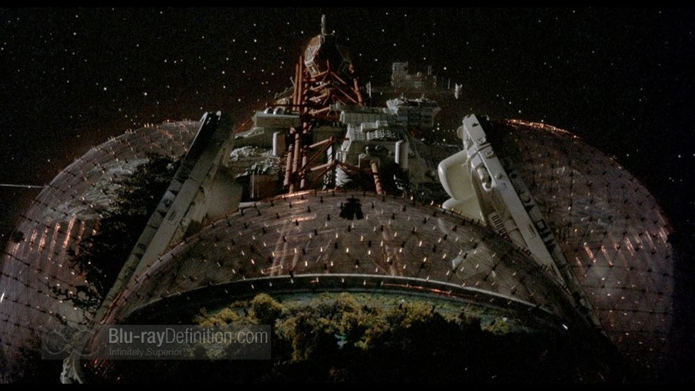 A complex spaceship consisting of transparent habitat domes criss-crossed with an array of lights over living trees, all connected to a central cluster of complex structures