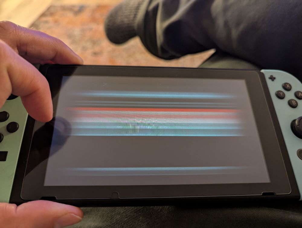 A switch resting on my lap 
The screen is showing horizontal stripes of various colors, including red, white, blue, and black.