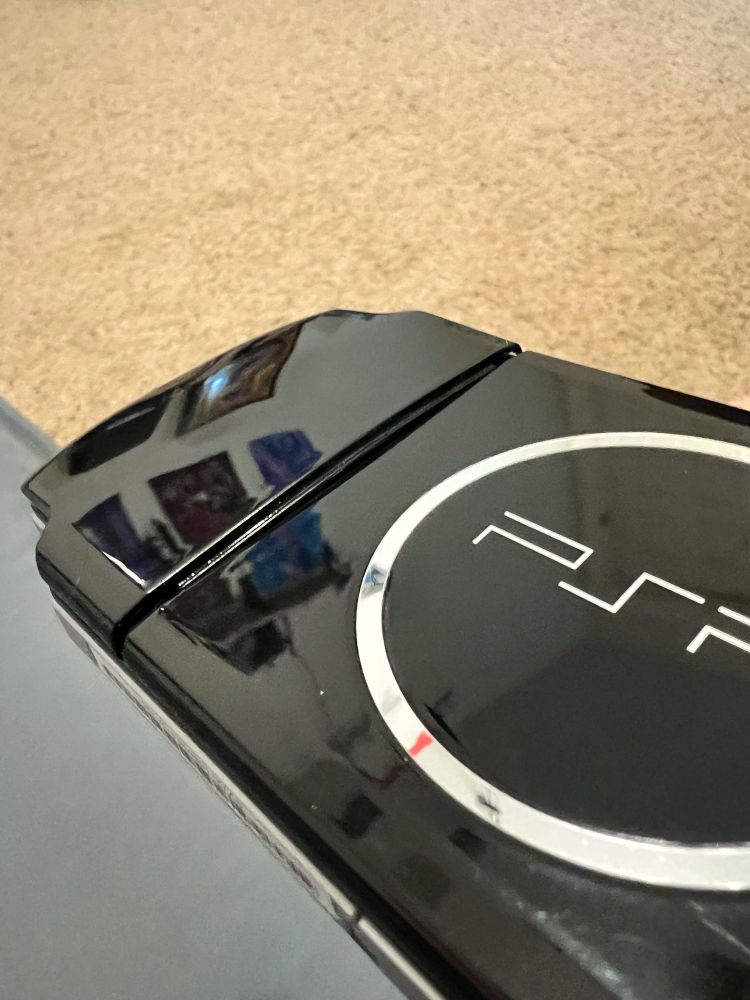 The back of a PSP (PlayStation Portable) with the battery compartment slightly bulging due to the old lithium ion battery swelling up.