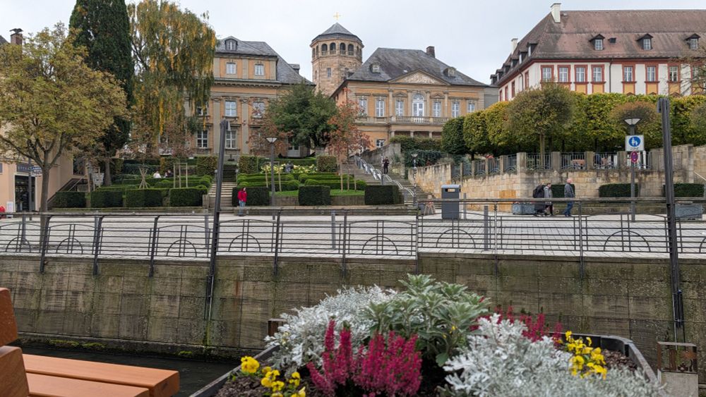 Im Vordergrund Blumen, im Hintergrund ein Hügel mit gediegenen Gebäuden 