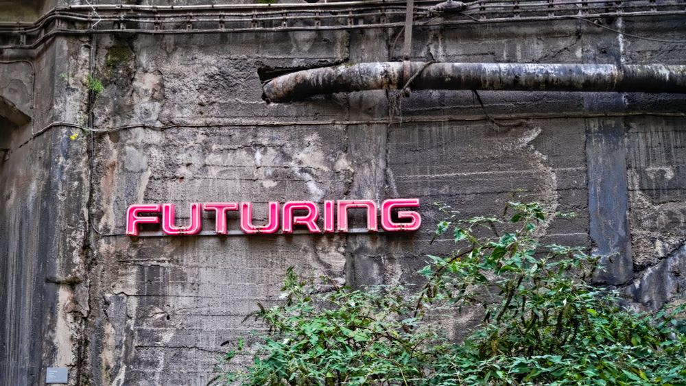 Das Foto zeigt ein altes, rau verputztes Gebäude, dessen Oberfläche Risse und Flecken aufweist. In der Mitte des Bildes leuchtet eine rote Neon-Schrift, die das Wort 