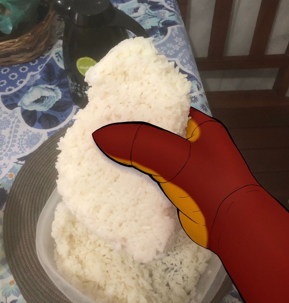 A photo of a hand holding a block of cooked rice. The sticked on one another, and now they create a huge piece of rice. The hand is drawn over to look like a character's over the real one.