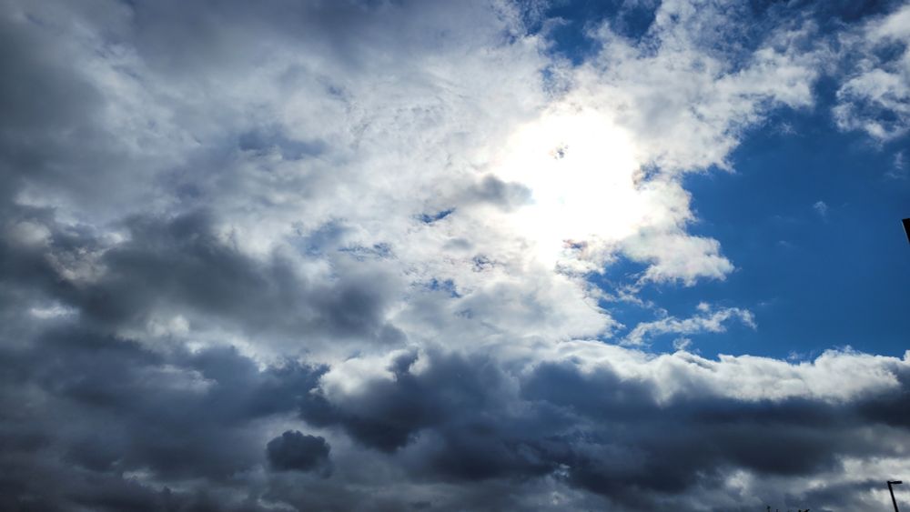 dark clouds in the bottom half and left side, with a slice of blue in the top right and the sun, bright but concealed by cloud