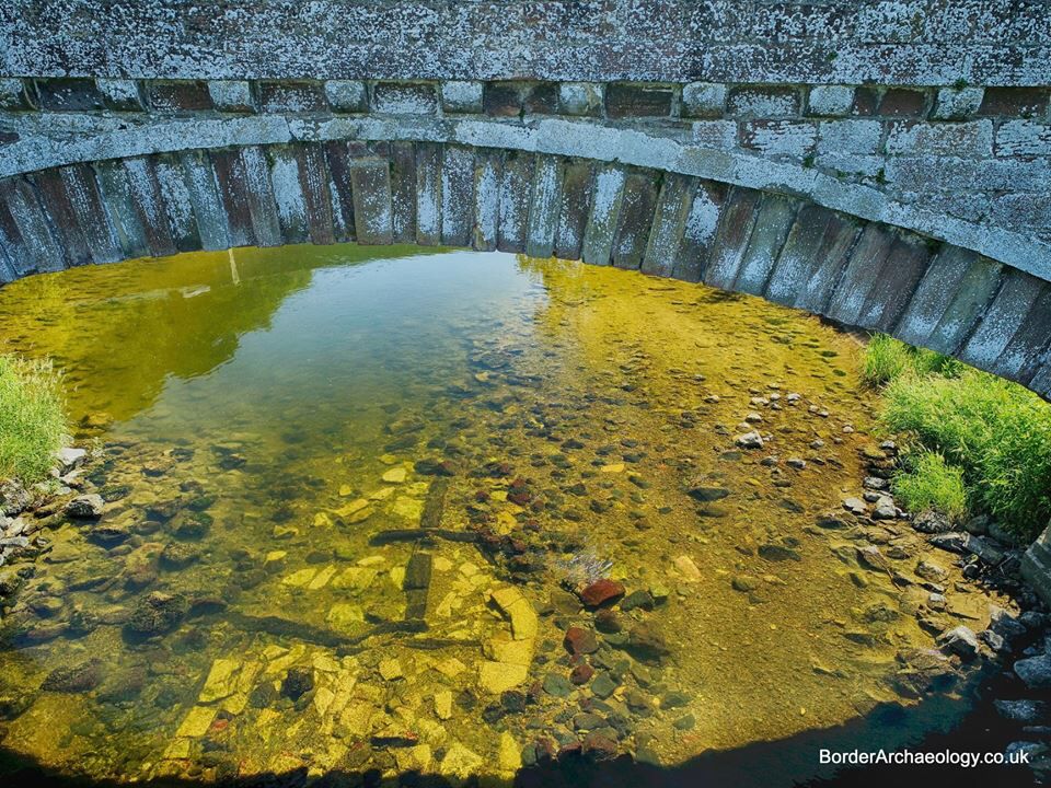 Drone photo of timber framework within stone pier base remains in floor of river Teviot under extant later 18thC bridge - photo by the late Richard Strathie a member of Ancrum & District Heritage Society.