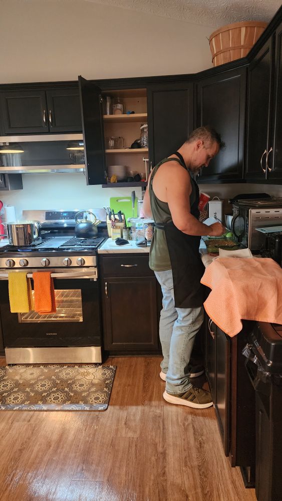 Brandon in the kitchen making greenbean casserole. A pot is on the stove behind him. He's wearing an apron. 