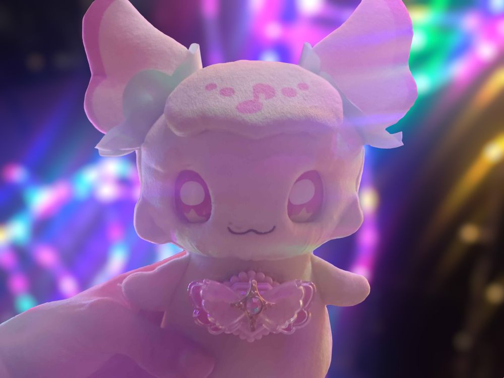 a Purirun eye blinking talking plush behind some christmas lights with bokeh blur effect on, fairy character from the Anime You and Idol Precure (Kimi to Idol, Kimipre)