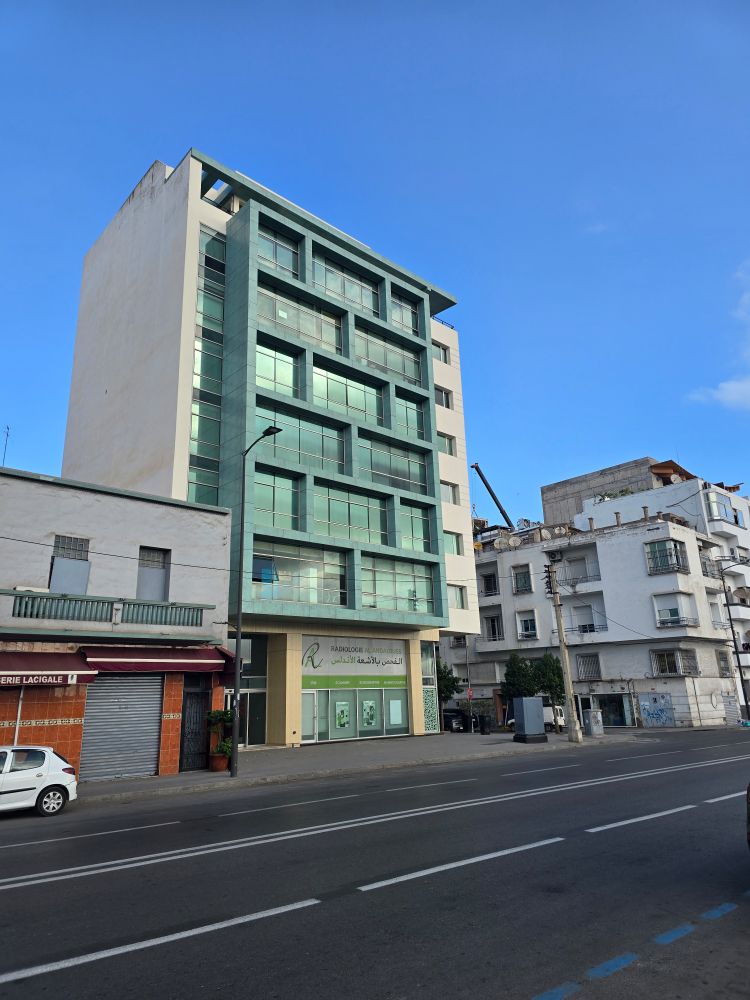 A modern, squared off apartment next to a shorter, squatter concrete building.