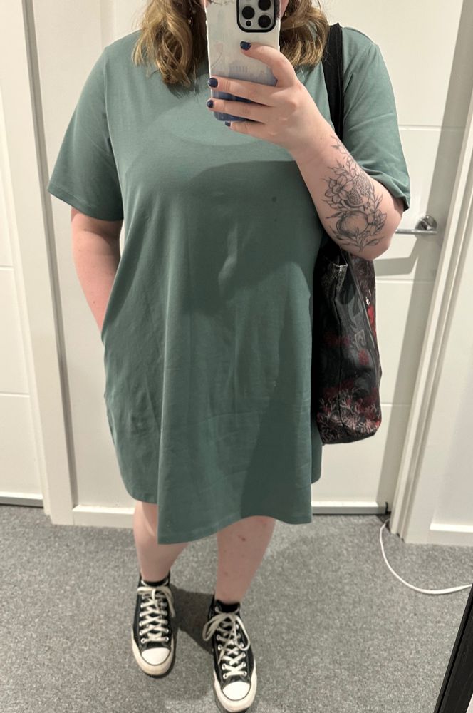 A person in a long tshirt dress taking a selfie in the mirror