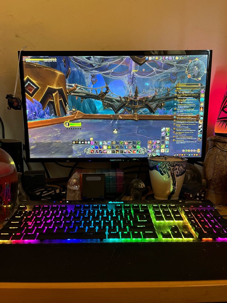 My computer setup with WoW screen, rogue character. Rainbow mechanical keyboard, and accompanying mug of coffee.
