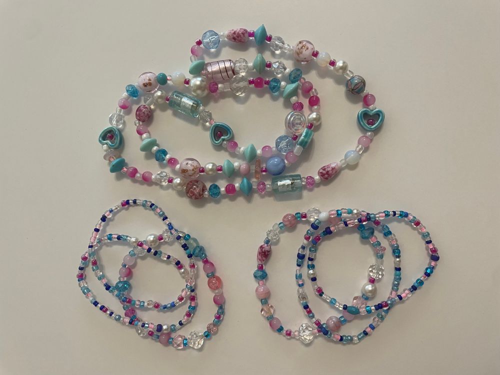 A necklace and two sets of three beaded bracelets in shades of pastel blue and pink, made from recycled beads 