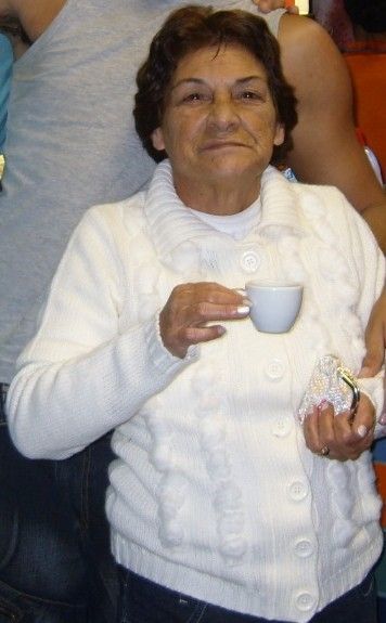 Minha mãe, meu amor. Ela tinha 1,50m de pura ousadia. Os cabelos castanhos curtos, os olhos sorrindo, um sorriso de boca fechada. Pele morena curtida de sol. Uma xícara de café na mão direita e uma bolsinha de moedas na mão esquerda. Ela veste uma blusa de lã branca com grandes botões também brancos.