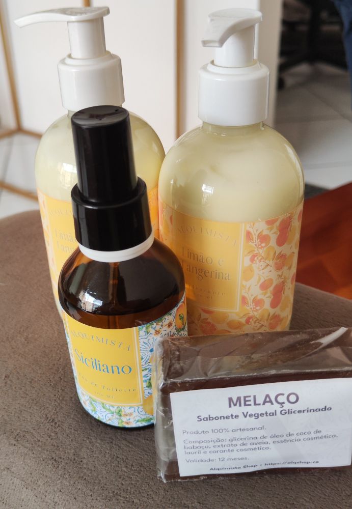 Produtos da Alquimista que acabaram de chegar. Um sabonete de melaço em barra à direita, de cor marrom; um eau de toilette de limão siciliano no meio, em embalagem marrom e dois hidratantes de limão e tangerina mais ao fundo, em embalagem transparente. Tudo absurdamente cheiroso.