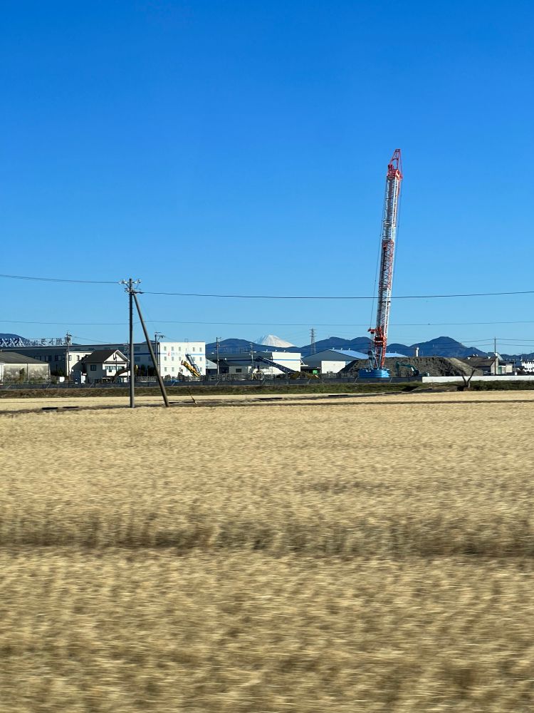 A field flashes by in rural Japan and Mount Fuji ducks behind a building in the distance.