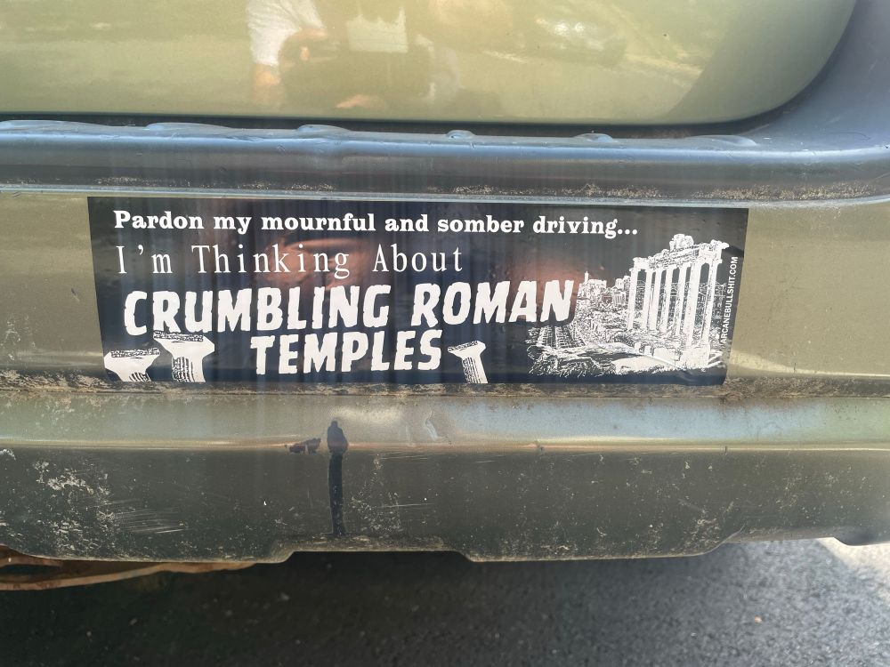 Bumper sticker on a green car that reads “pardon my mournful and somber driving…I’m thinking about crumbling Roman temples”