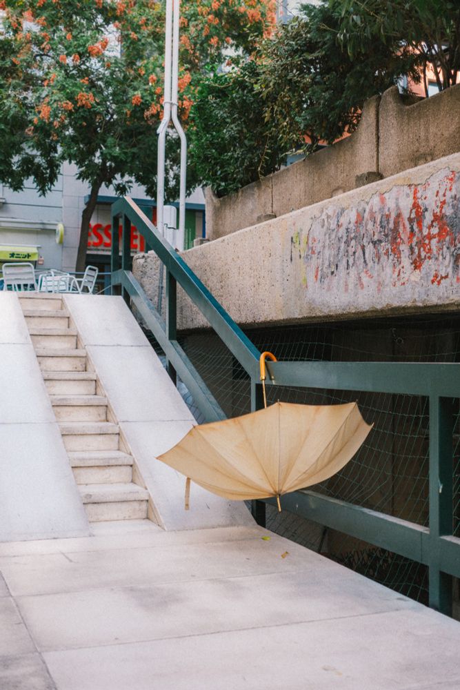 Un paraguas blanco de color crema cuelga abierto de una barandilla verde.