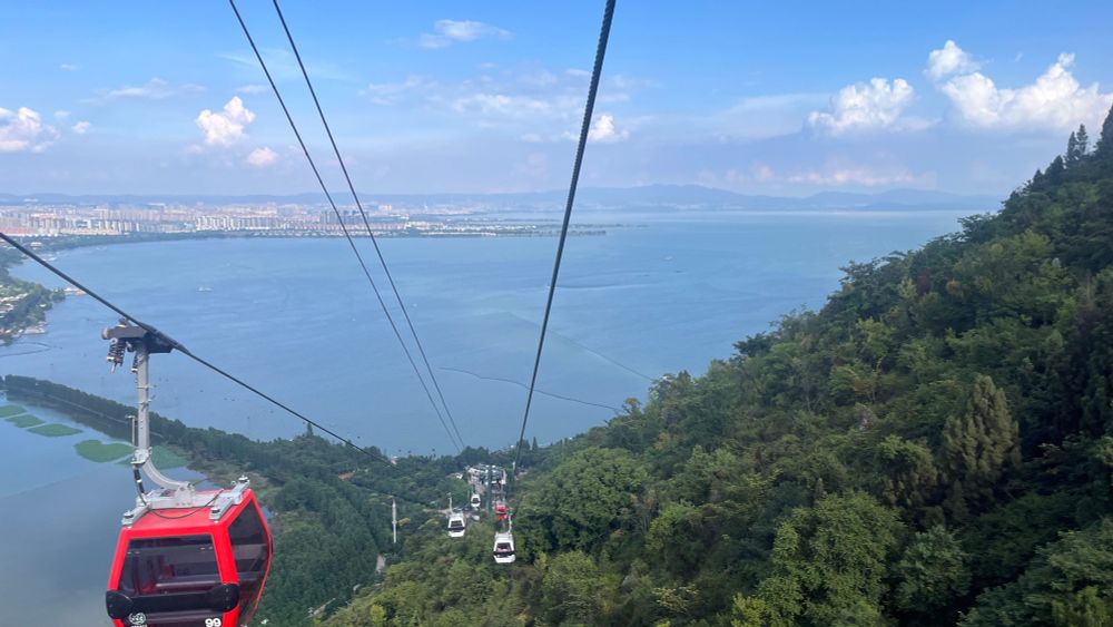view outside a gondola going down a steep hill with a big lake in the distance