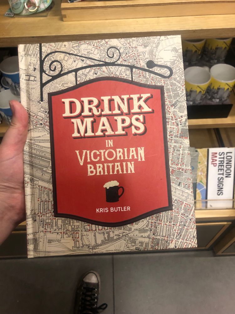 A book entitled “Drink Maps in Victorian Britain”. The cover has the title inside a traditional sign found outside a pub, while the background is a map of London in Victorian times 