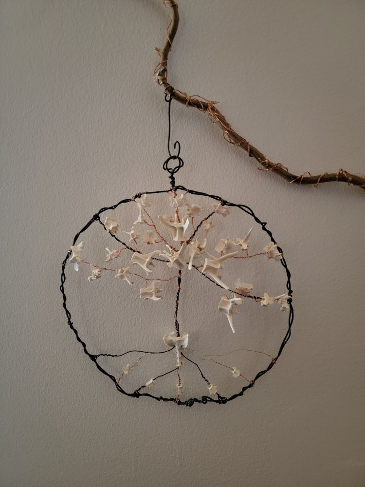 A wire rapped circle with wires in this shape of a tree and bones wrapped on with wire in place of leaves and along the roots.