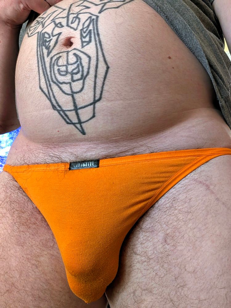 A close up view of AJ's stag tattoo and package wrapped in orange briefs.