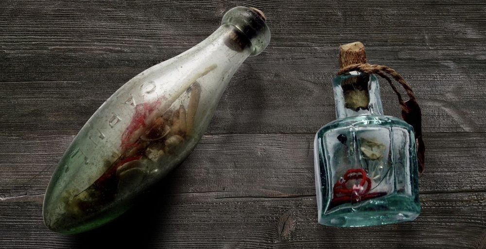 two witch bottles on wooden table filled with bones and string as a folklore practice