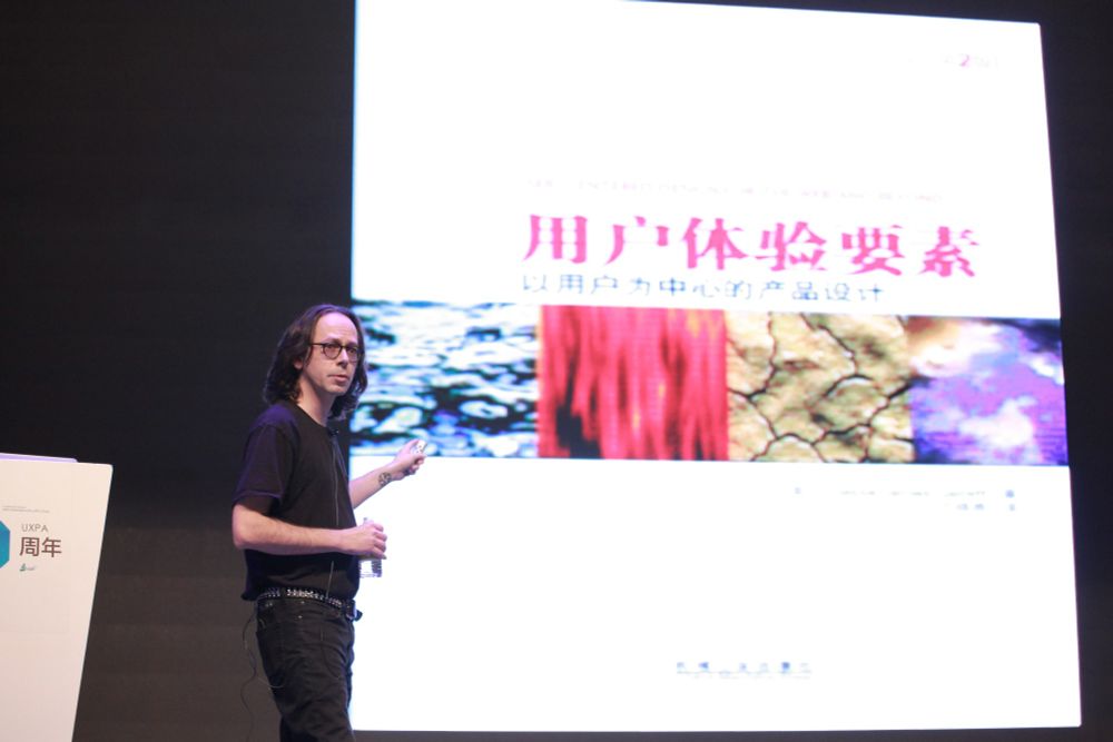 Jesse James Garrett onstage with an image of the Chinese edition of The Elements of User Experience.