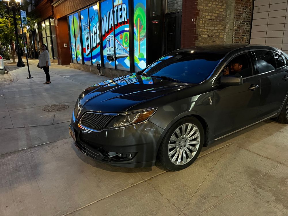 A vehicle parked lengthwise across the sidewalk and blocking it in front of an L station on Chicago. 