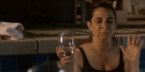 Maya Rudolph in a pool with a wine glass, her eyes are closed and she puts her hand over her heart