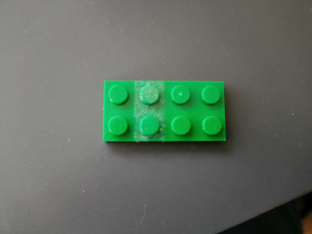 Photo of a 2x4 Lego piece. Two of the studs are very dusty while the others are clean.