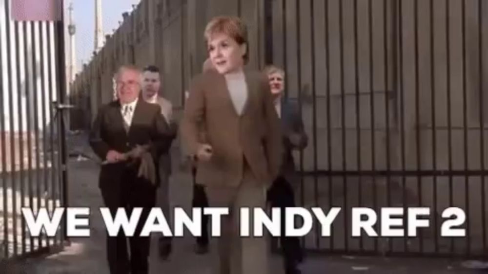 a group of people are walking down a street with the words `` we want indy ref 2 '' written on the screen .