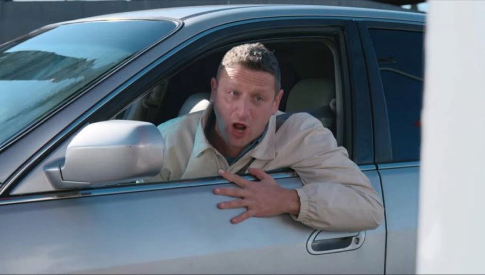 Tim Robinson leaning out his car window at a drive thru and yelling 