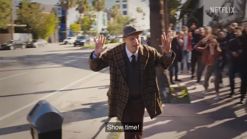 Tim Robinson as Richard Brecky/Jellybean, walking on a sidewalk and saying “show time” while raising his hands