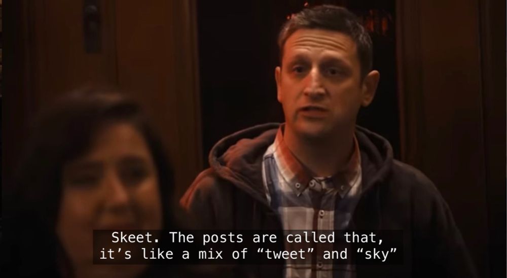 A closeup on Tim Robinson’s character. He has an innocent and earnest look on his face. He is saying “Skeet. The posts are called that, it's like a mix of ‘tweet’ and ‘sky’”