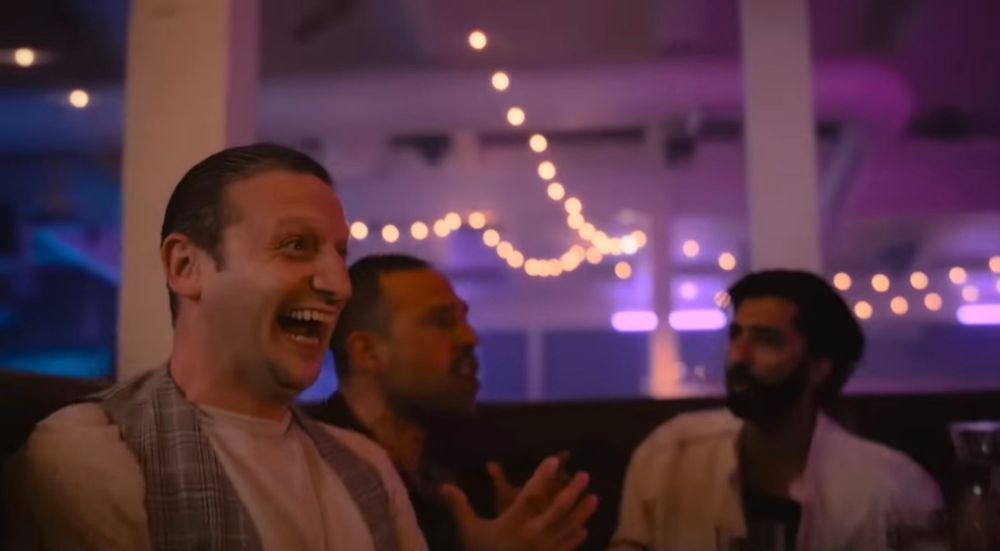 Tim Robinson with slicked-back hair, sitting at a booth with some other guys, laughing maniacally and smiling, in the Sloppy Steaks sketch from I Think You Should Leave