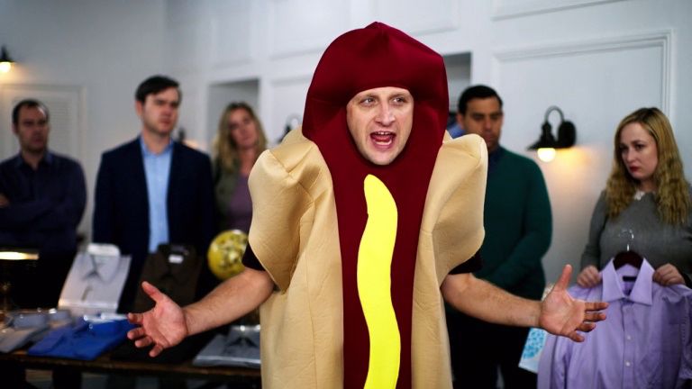 Tim Robinson standing in a hot dog costume with his hands out to the sides, exasperated
