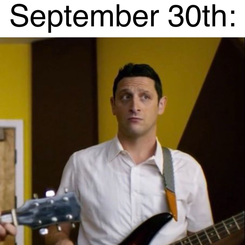 Tim Robinson in a recording studio, playing bass guitar with a casual expression