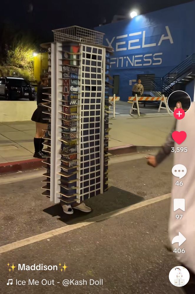 Screenshot of a TikTok taken at night centering someone’s Halloween costume. They are standing on a street dressed as one of the abandoned luxury towers in LA that were graffiti bombed earlier this year. Their shoes can be seen peeking out from below the costume, which otherwise encases their entire body. 