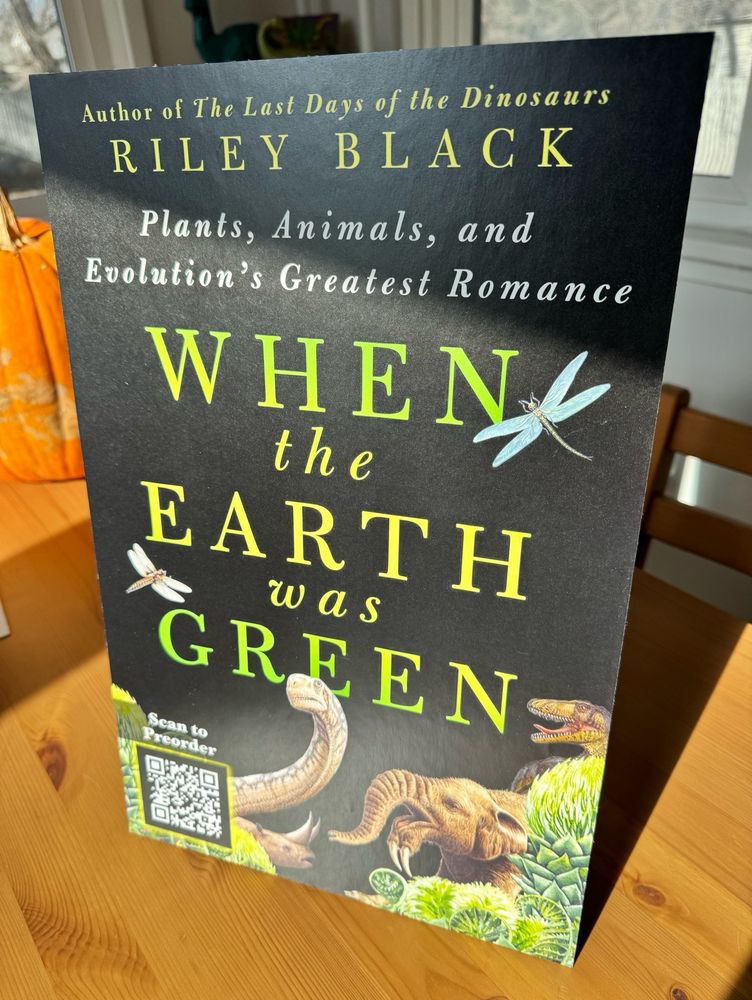 A standing display for Riley’s new book When the Earth Was Green, showing prehistoric animals and plants against a black background 
