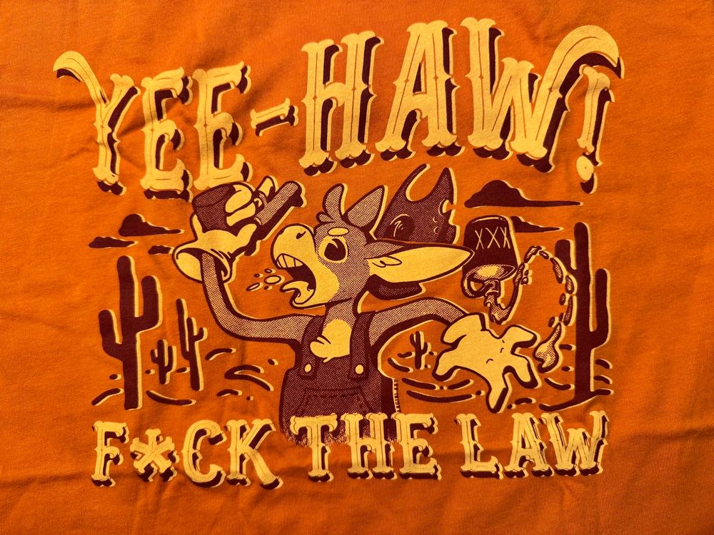 An orange shirt in a cartoon old west style that says “Yee-haw! F*ck the law.” with a gun-slinging donkey with some XXX liquor