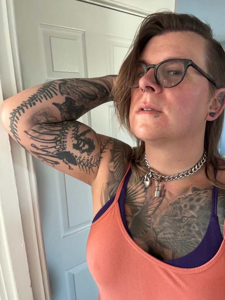 Riley in a peach cami showing her arm muscles. It’s covered in animal and bone tattoos.