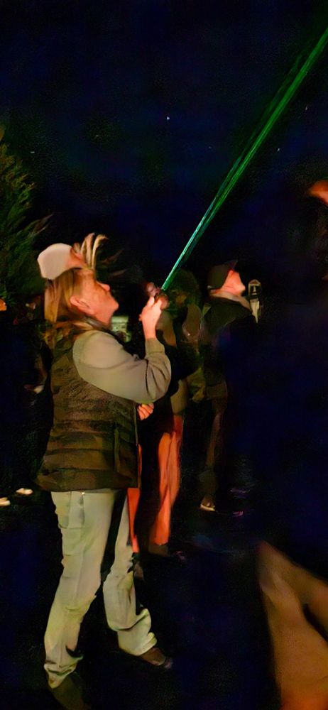 Lady shining a laser been into the night sky among watching crowd.