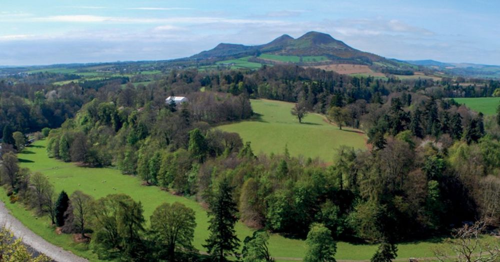 This picture shows the Mid and South Eildon Hills from a view of the Tweed River. The hills are green with trees leading across them.