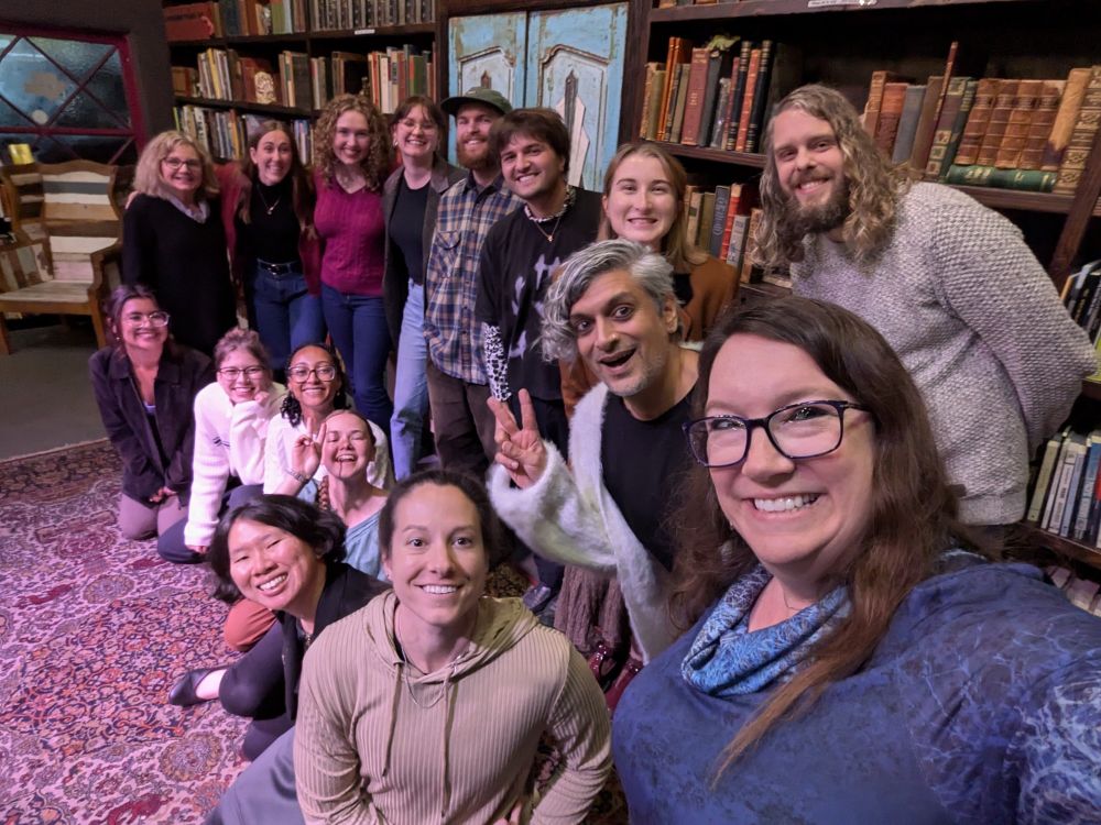 a selfie of a group of smiling people in two rows in front of a big bookshelf