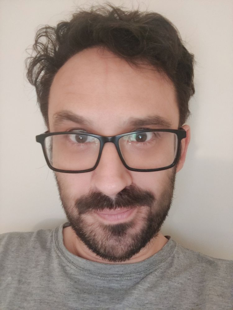 A picture of me with spectacles, a beard & moustache, wearing a grey t shirt. I have dark, messy hair